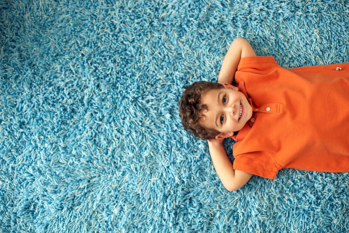 A young child relaxing on a freshly cleaned blue carpet after Eco Valley Chem-Dry’s professional carpet cleaning service, showing a safe and healthy space free from pet urine odor removal concerns and deep carpet contamination.