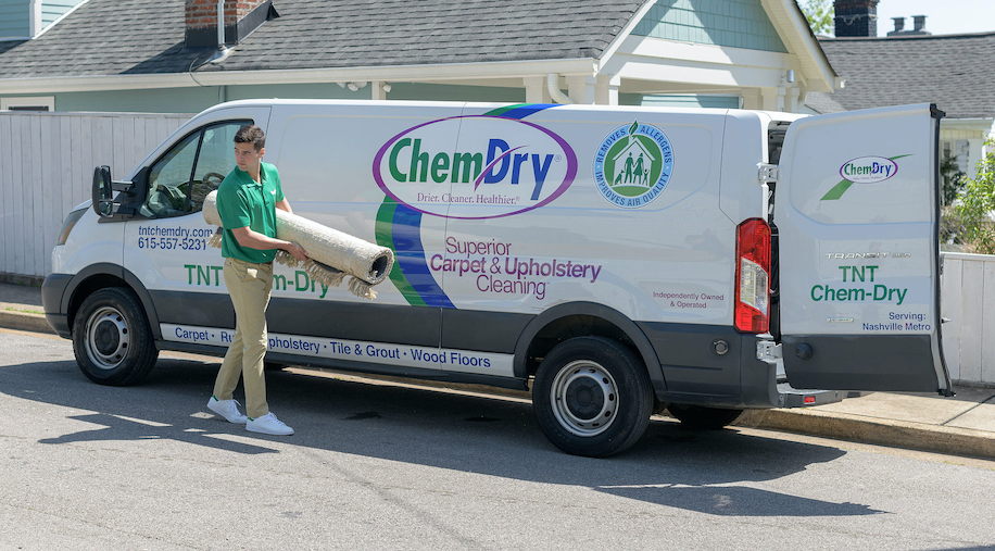Chem-Dry carpet cleaning technician unloading equipment from a service van outside a residential home, preparing for fast on-the-spot carpet cleaning
