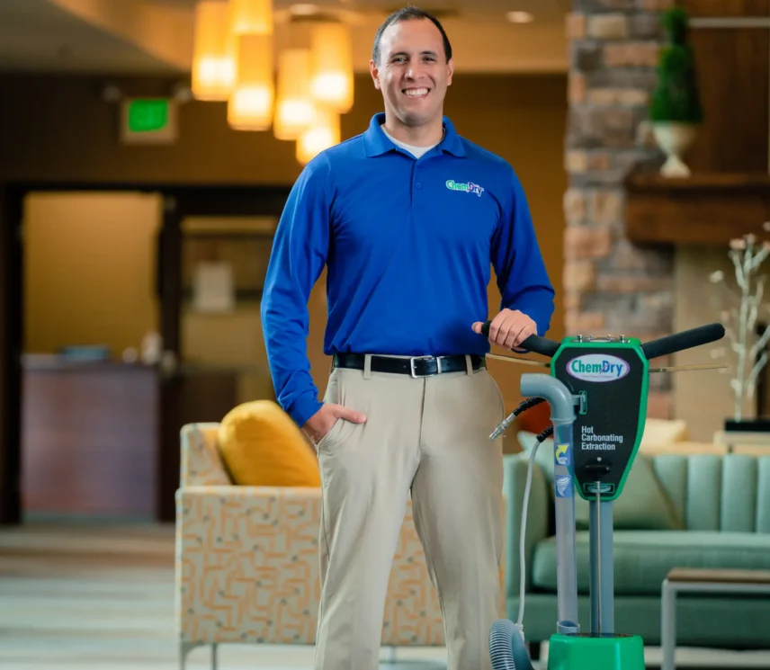 Professional upholstery cleaning technician standing with a portable spot cleaner machine in a residential living space
