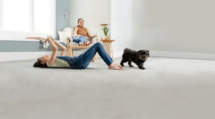 Family and pet relaxing on a clean carpeted floor in a bright living room, representing a fresh home environment after professional pet urine odor removal and carpet cleaning
