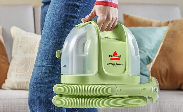 Hand holding a portable Bissell upholstery cleaner machine for spot cleaning furniture and carpets