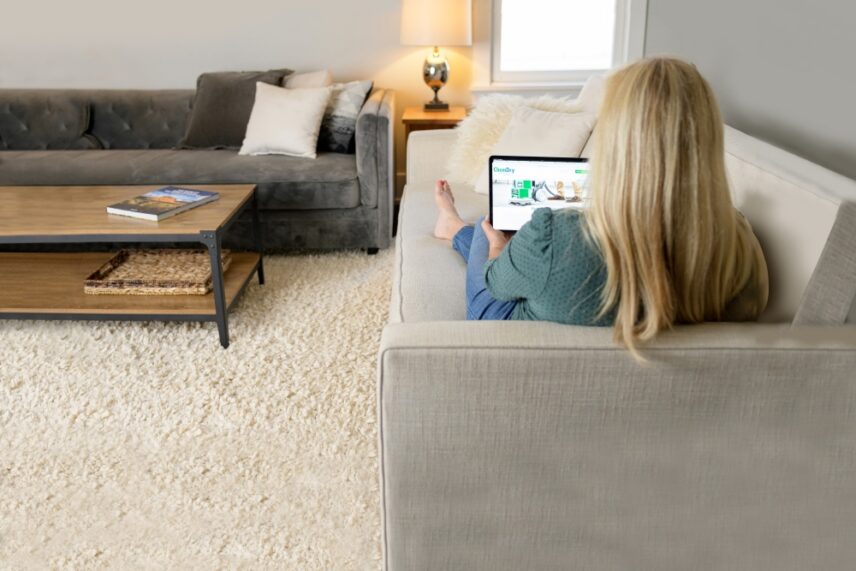 Woman relaxing on a clean sofa using a tablet in a fresh living room after professional upholstery and carpet cleaning service