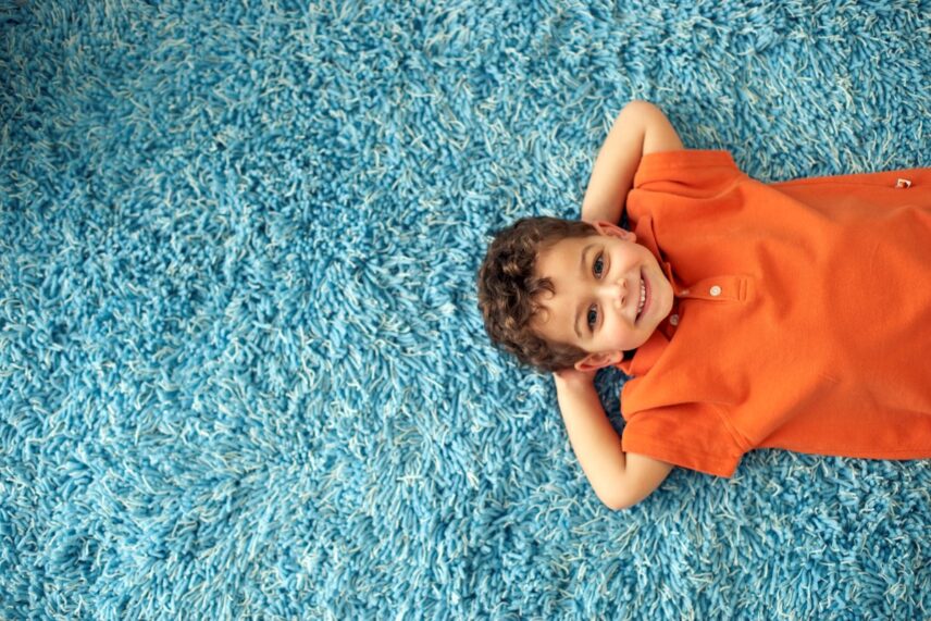 Child lying on a bright blue shag carpet smiling, representing a clean and freshly maintained carpet suitable for professional carpet cleaning services