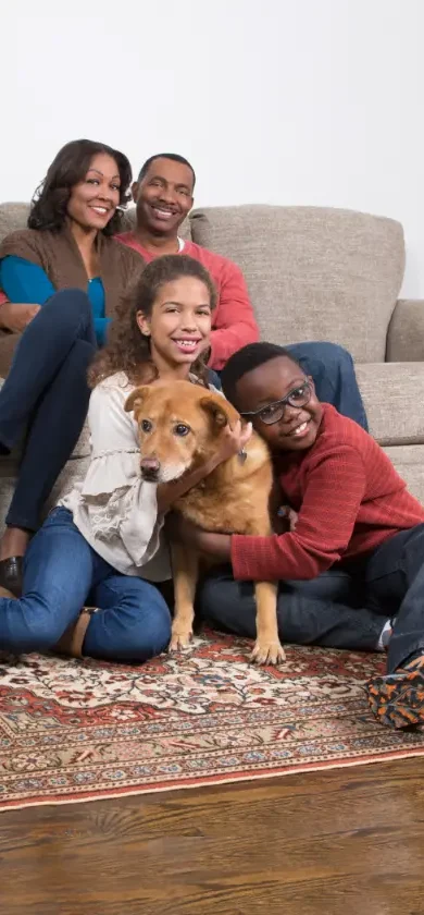 Happy family relaxing with their dog on a clean rug after professional Pet Odor Cleaning Services, creating a fresh and healthy home environment